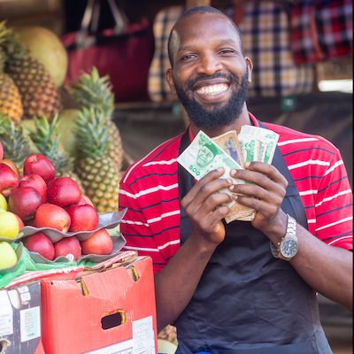 Male market vendor counting money beside a colourful fruit display, authentic local market scene